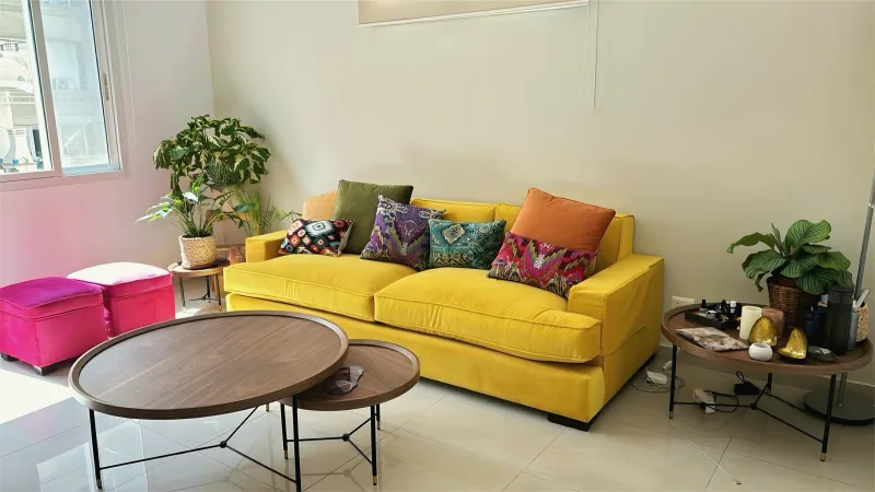 Living room with a yellow sofa and round coffee tables by Yamout