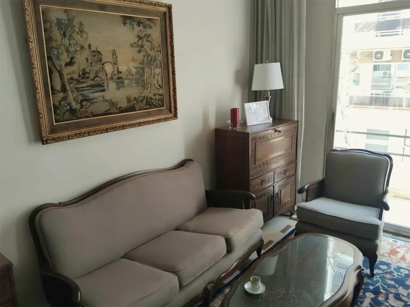 Living room with a carved wood sofa, a framed tapestry and a glass coffee table, by Yamout