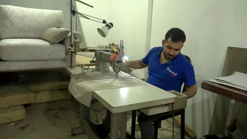 A Yamout upholsterer at the sewing table, a finished sofa behind him